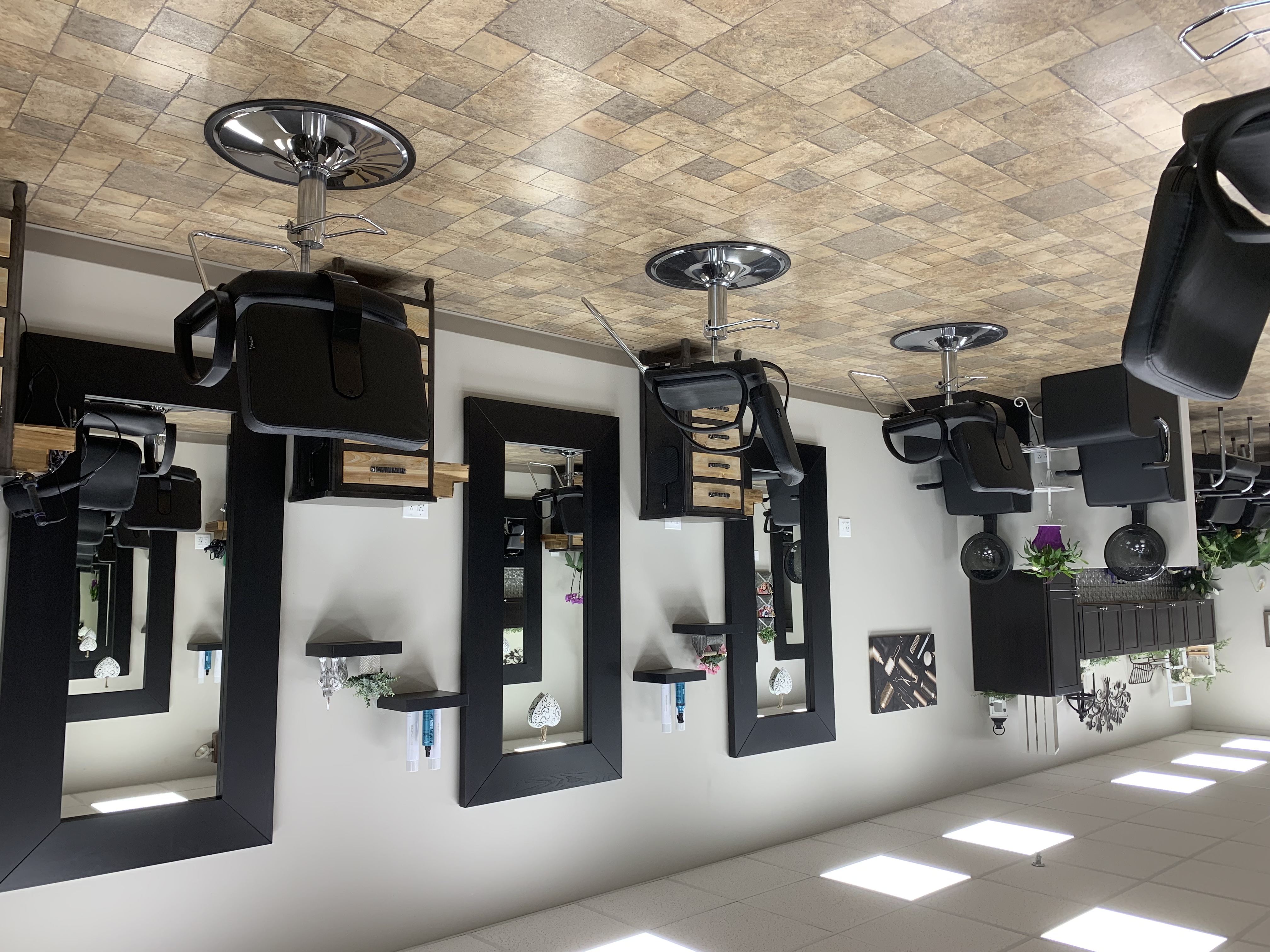 Multiple hair salon stations with black chairs and mirrors, tile floor, and ample lighting